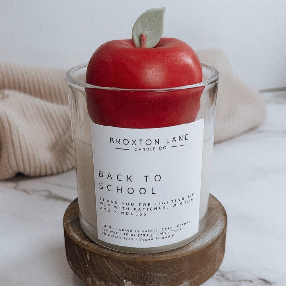 Candle with a red apple on top labeled 'Back to School' by Broxtone Lane on a marble surface.