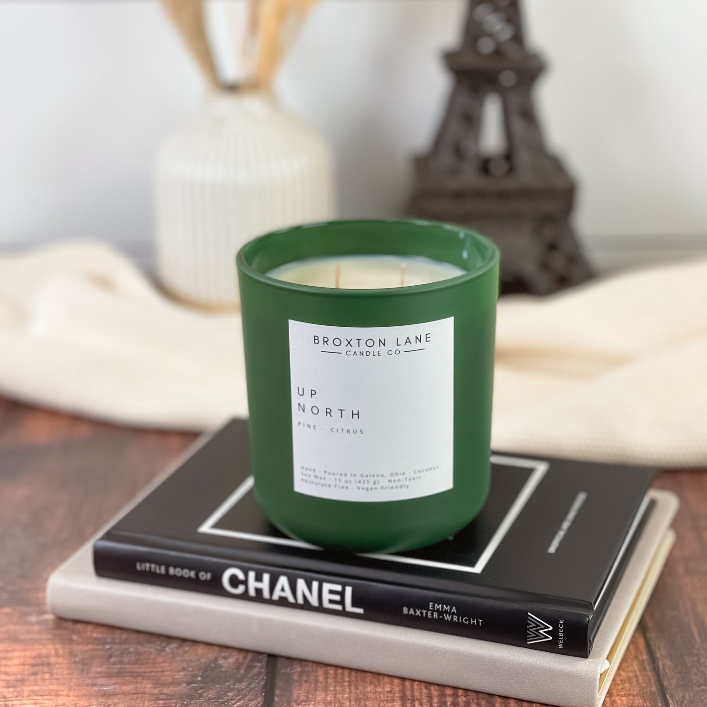 Green candle with a label on top of a Chanel book on a wooden surface.