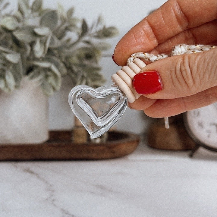 Hand holding a small heart-shaped object with a marble surface and plant in the background