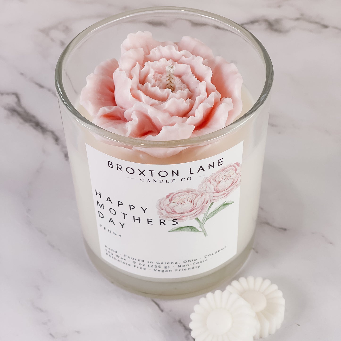 Candle with a pink rose design and 'Broxton Lane' label on a marble surface