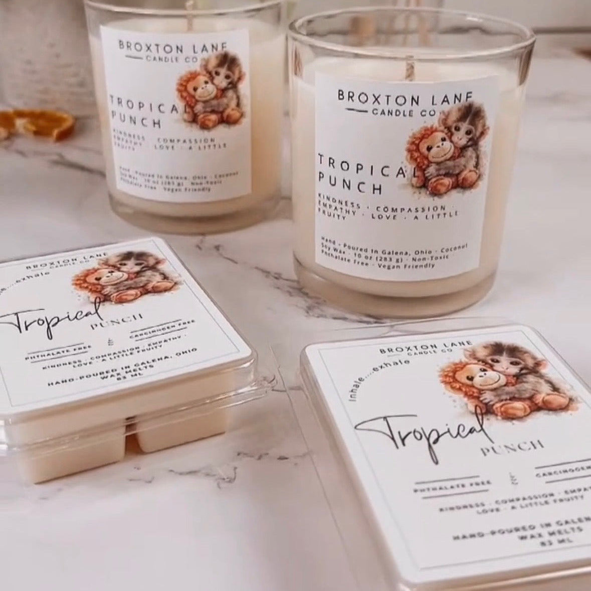 Two 'Tropical Punch' candles with lion graphics on labels, surrounded by packaging on a marble surface.