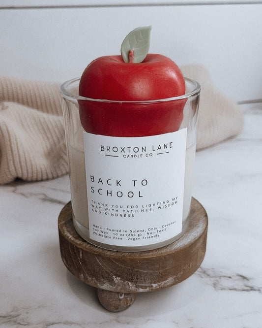 Candle with a red apple on top labeled 'Back to School' by Broxtone Lane on a marble surface.