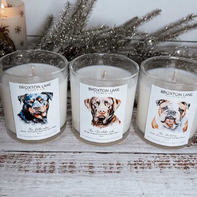 Three candles with labels featuring dog images on a wooden surface.