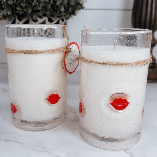 Two glass candles with red lip accents on a marble surface.