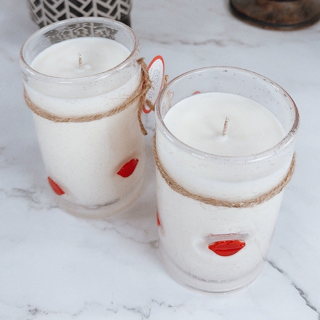 Two candles in glass jars with decorative lips on a marble surface.