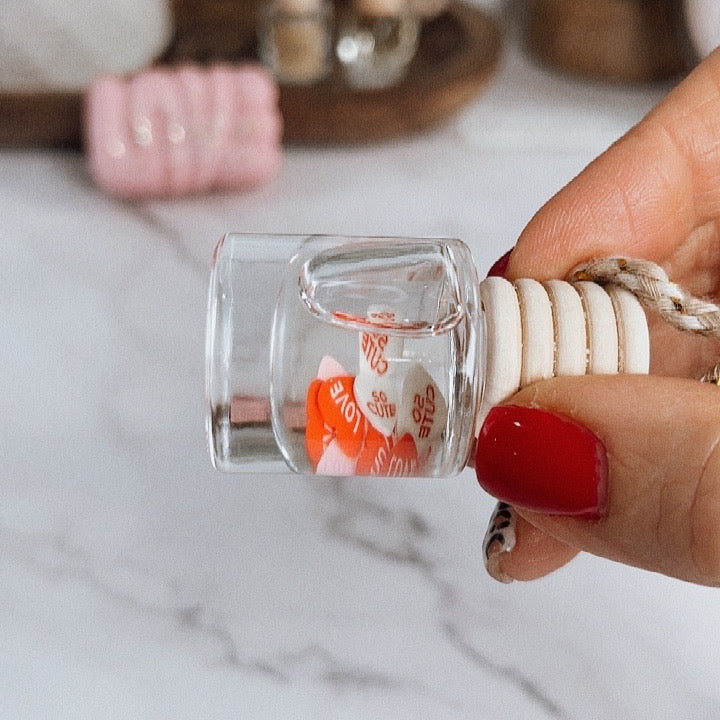 Hand holding a small glass bottle with a decorative item inside against a marble background
