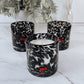 Candle in a leopard print container with decorative cherries on a marble surface, surrounded by plants.