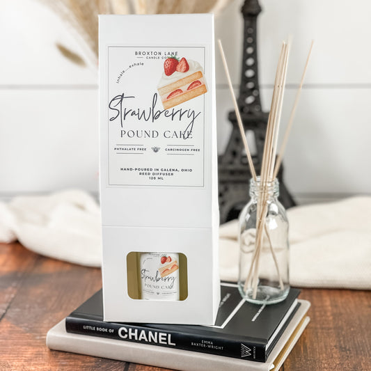 Strawberry pound cake diffuser packaging on a wooden surface with a Chanel book and decorative items in the background.