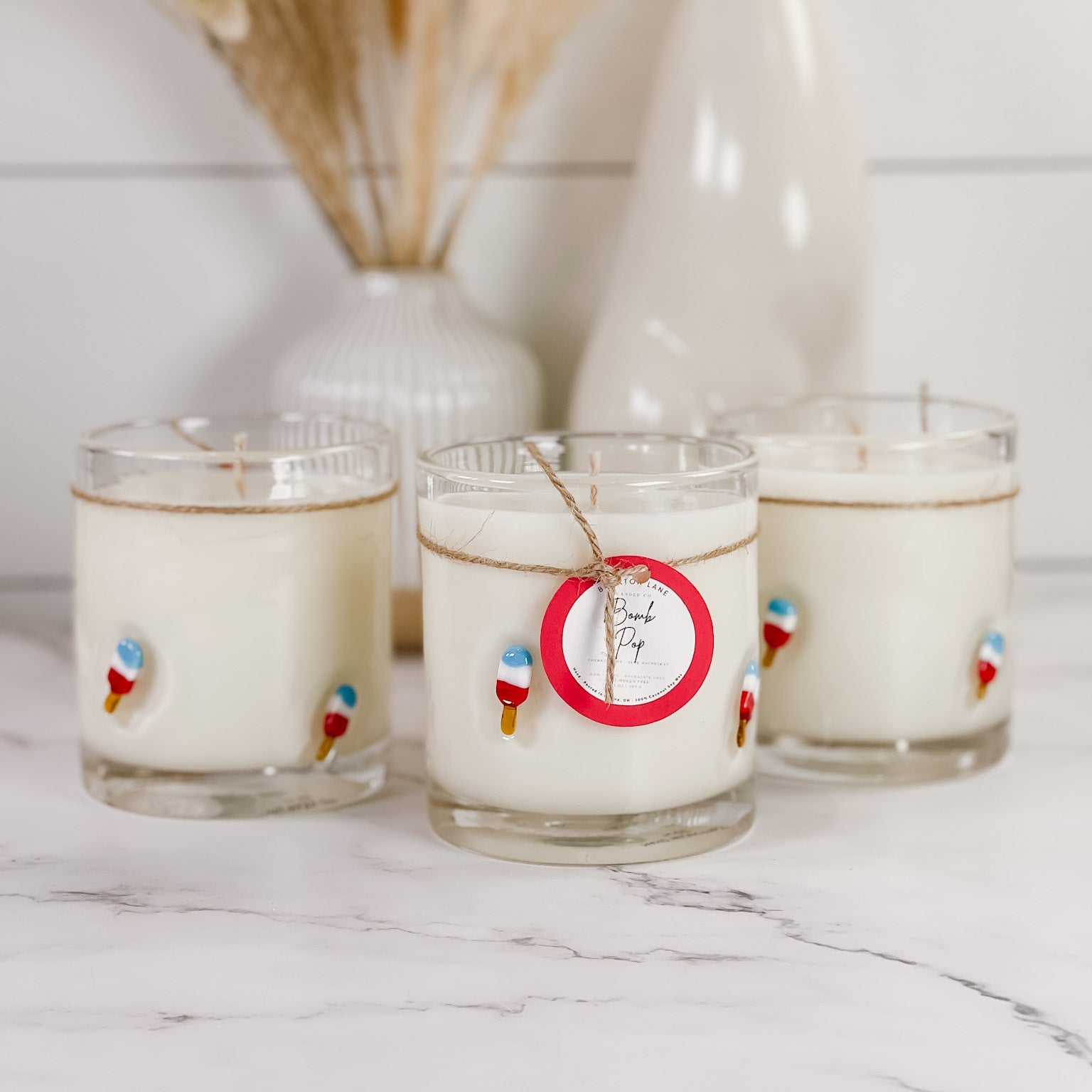 Three glass candles with decorative tags on a marble surface.