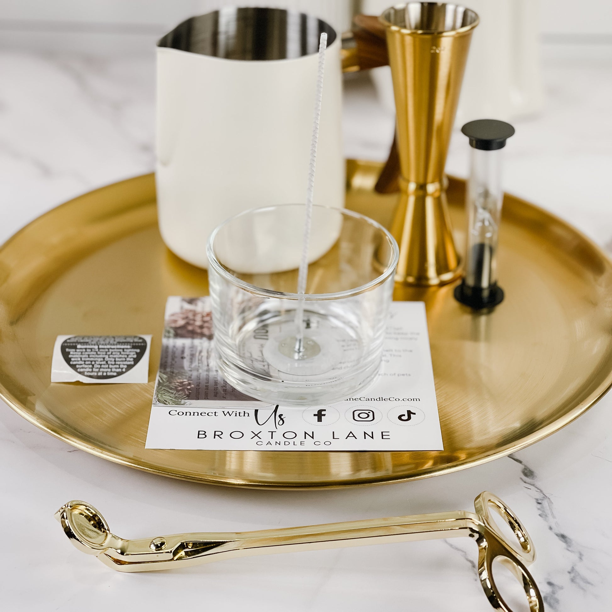 Candle-making tools and materials on a gold tray with a marble surface