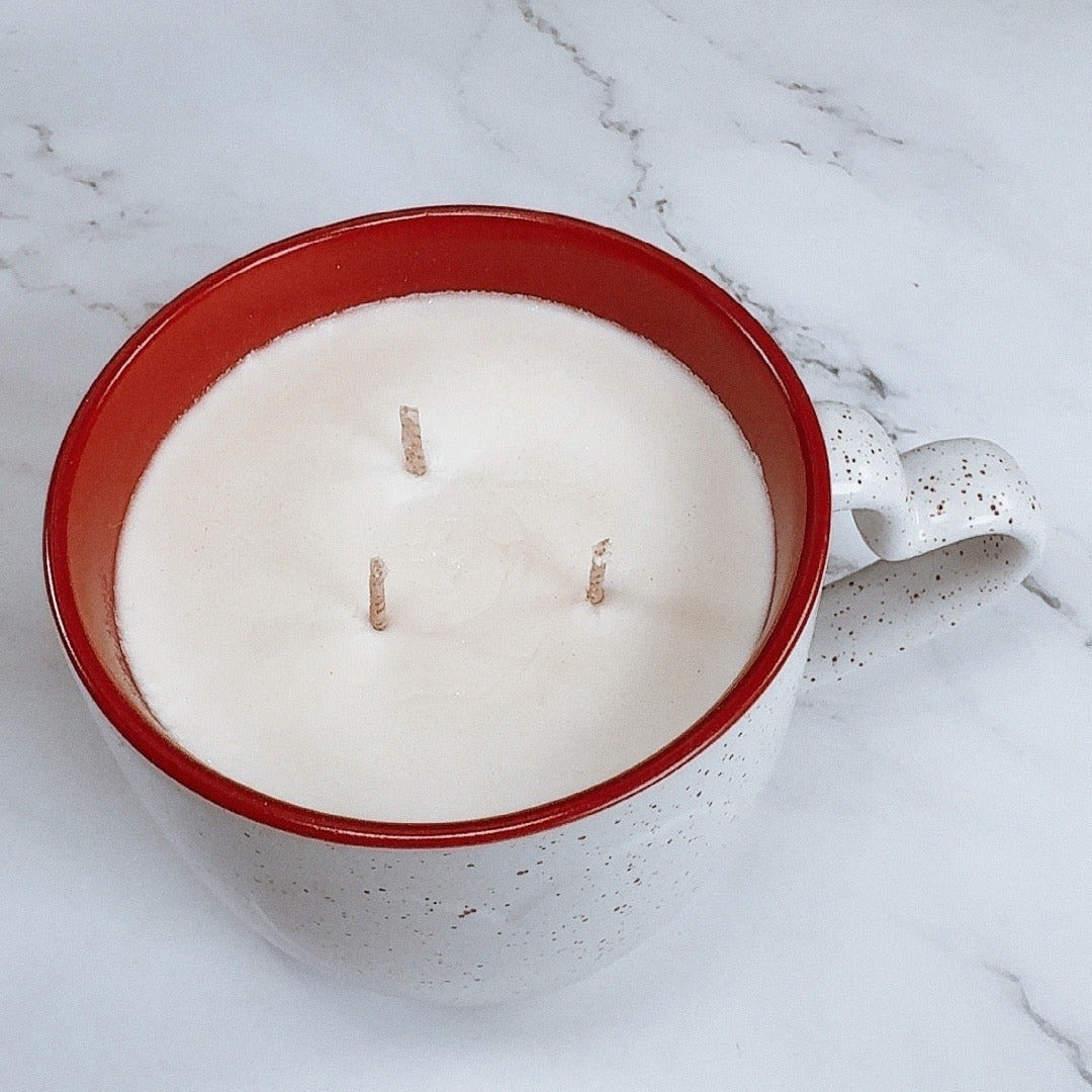 White candle in a red mug on a marble surface