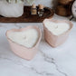 pink ceramic heart vessel with candle inside, on marbled table with decorative background
