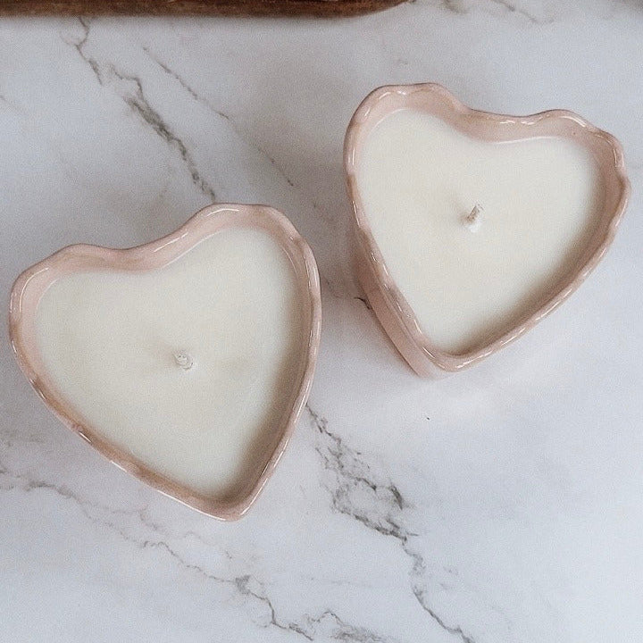 Pink ceramic heart vessel with candle inside on marbled table with decorative background