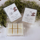 Two packages of coffee-scented wax melts on a white surface with greenery.