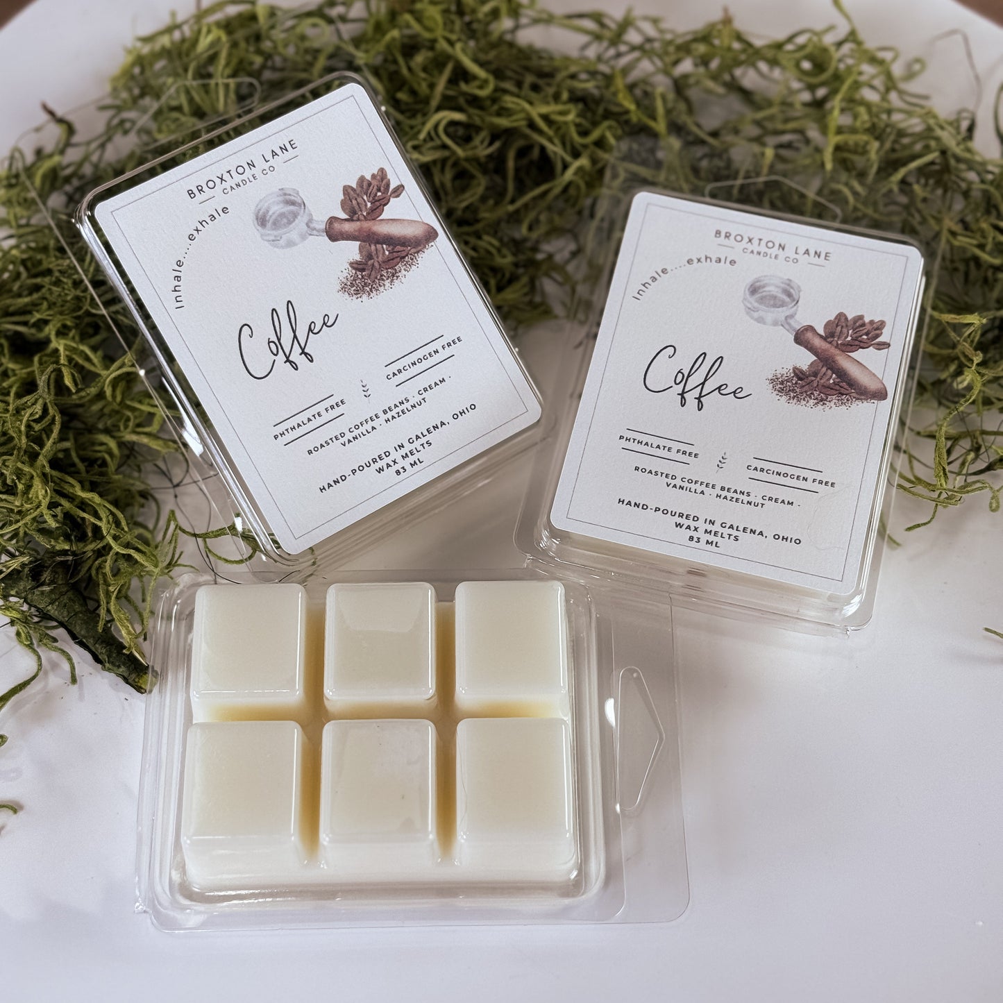 Two packages of coffee-scented wax melts on a white surface with greenery.