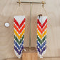 Colorful beaded earrings on a wooden stand against a light wood background