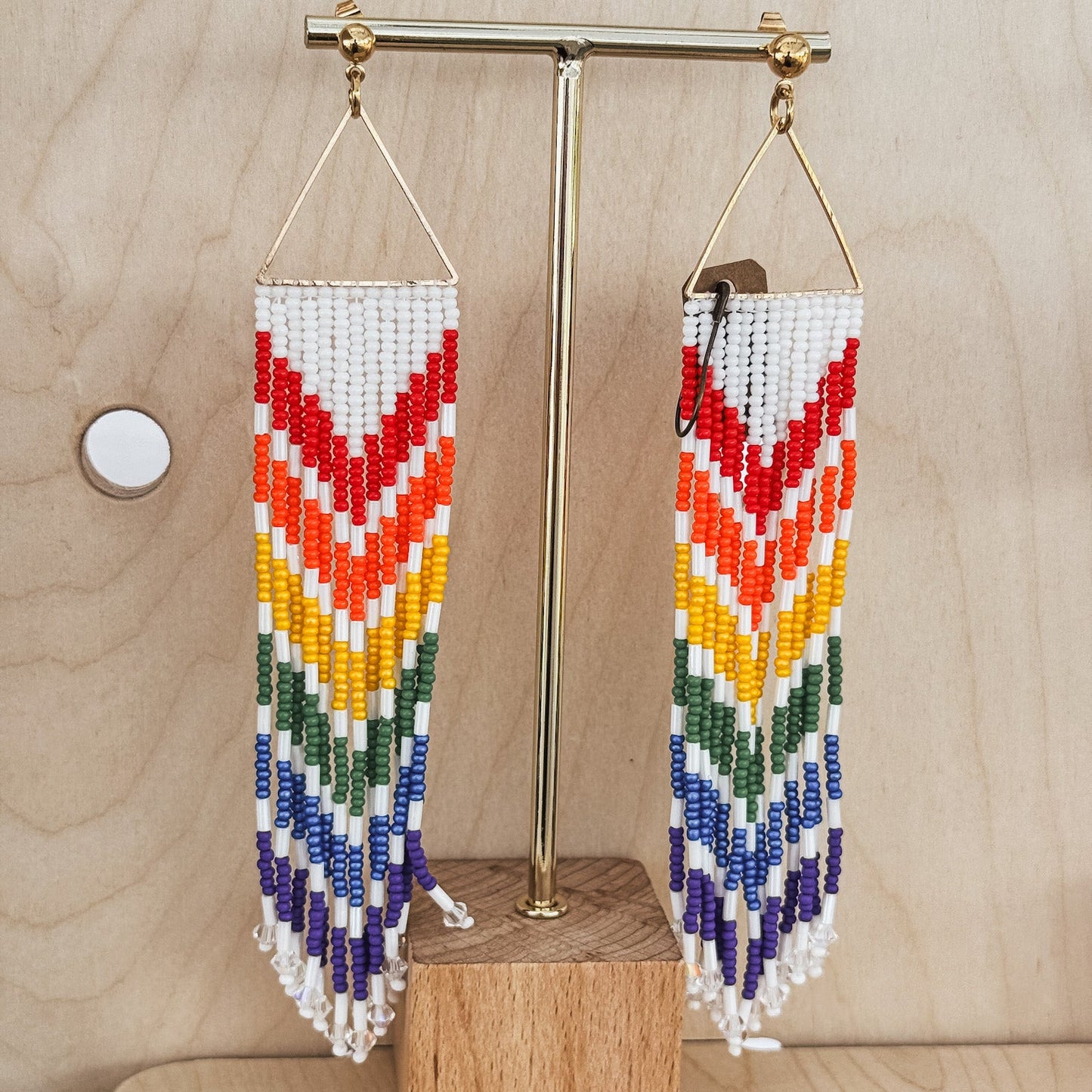 Colorful beaded earrings on a wooden stand against a light wood background