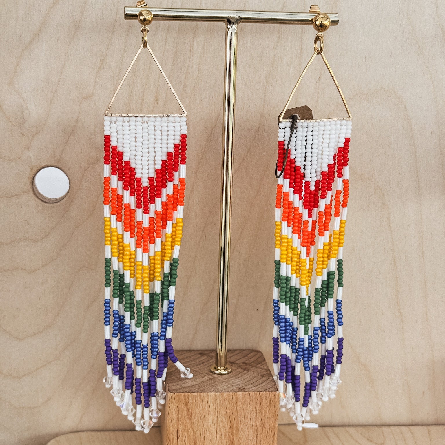 Colorful beaded earrings on a wooden stand against a light wood background